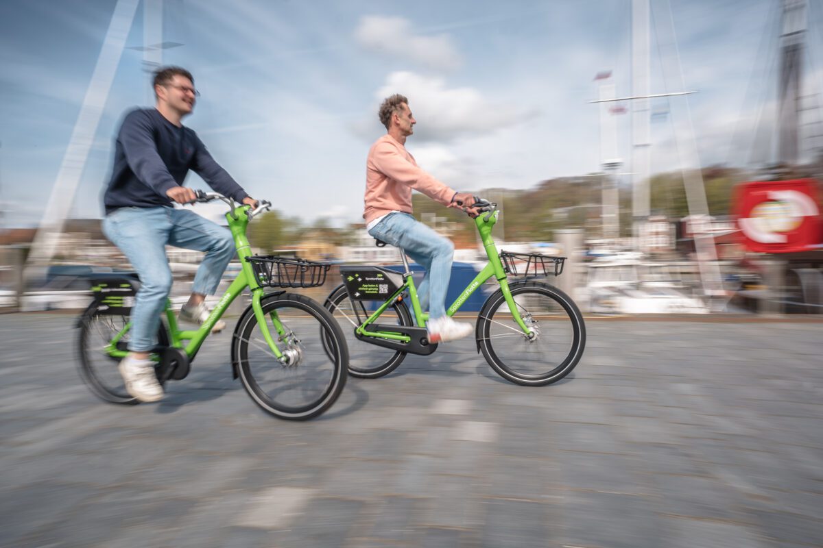 Zwei Personen fahren mit grünen SprottenFlotte-Leihrädern durch die KielRegion